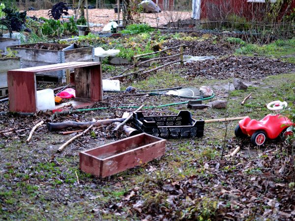 Redskap, träramar och leksaksbilar ligger utspridda i trädgården.