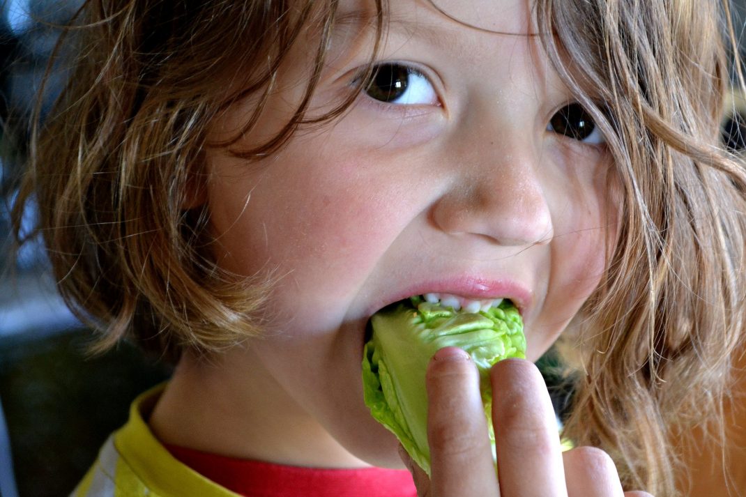 En pojke med långt hår äter sallat.