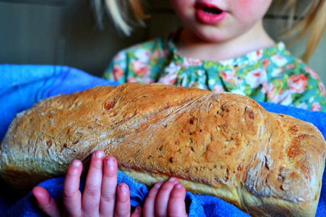 En liten tjej håller ett stort formbröd i famnen. 