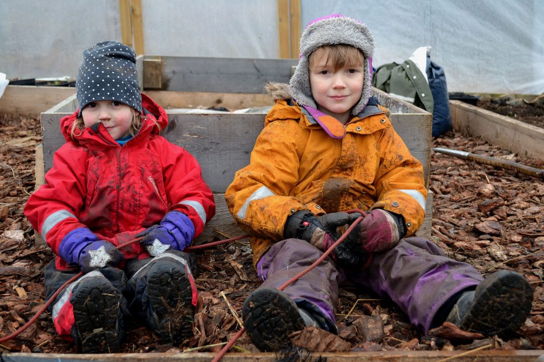 Barn i vinterkläder sitter i tunnelväxthuset. 