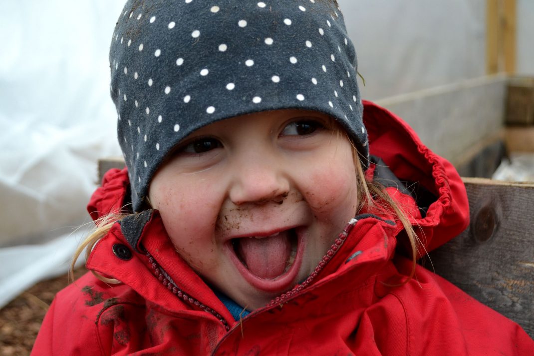 Ett barn med massa lera i ansiktet skrattar. 