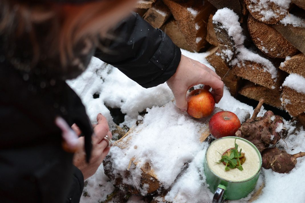 En kvinna arrangerar äpplen på en snöig vedhög.