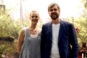 Sara och Johannes står bredvid varandra framför ett ljust växthus och grönska.