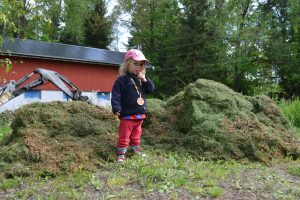En liten odlare framför en stor hög med gräsklipp.