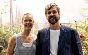 Sara och Johannes står bredvid varandra framför ett ljust växthus och grönska.