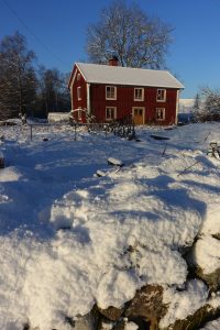 Vårt röda trähus omgivet av stenmur med snö på.
