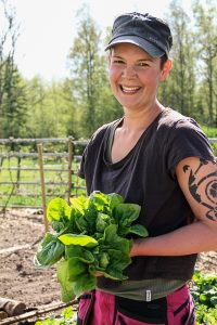 En glad Sara i keps håller ett stort knippe gröna blad.