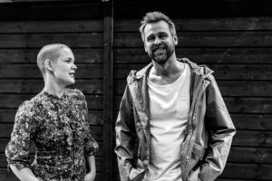 En svartvit bild av Johannes och Sara. Sara kollar på Johannes och säger någonting, Johannes tittar in i kameran och ler stort.
