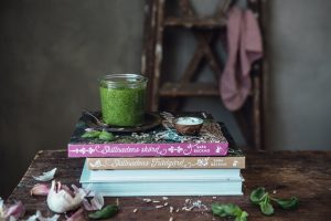 En härligt, grön pesto står i en glasburk på böckerna Skillnadens Trädgård och Skillnadens Skörd.