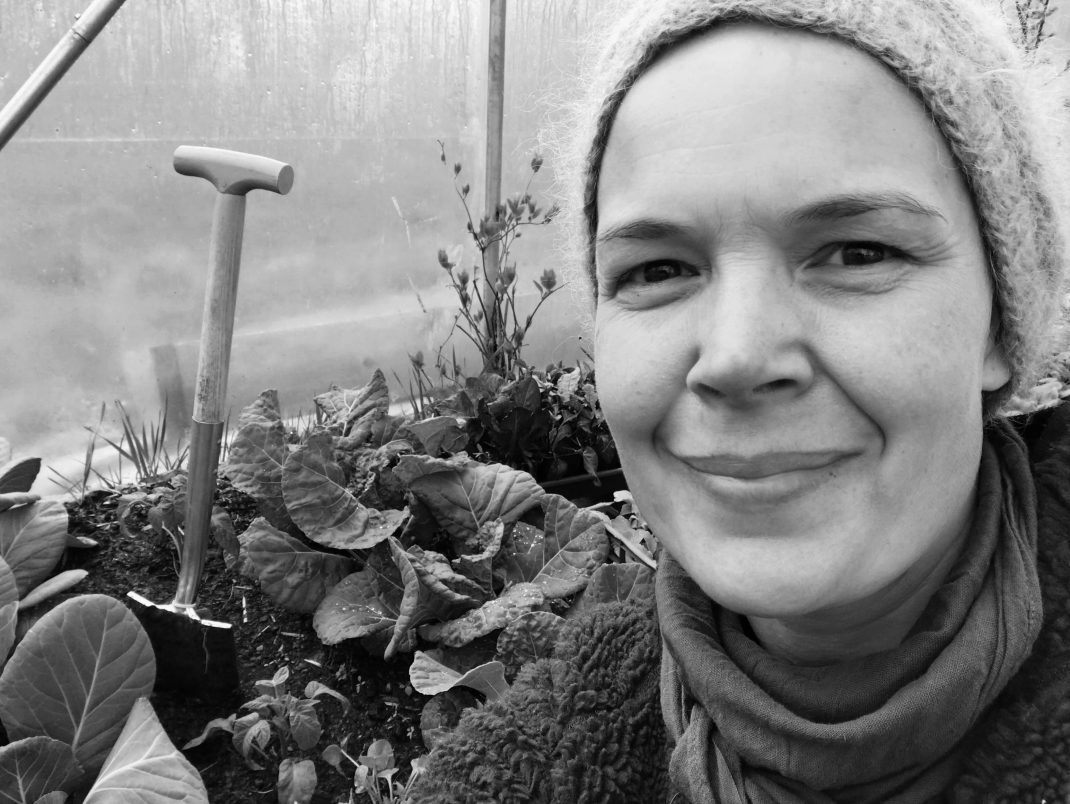 Svartvit bild av Sara i tunnelväxthuset. Bakom syns en liten spade och stora buckliga bladkål.