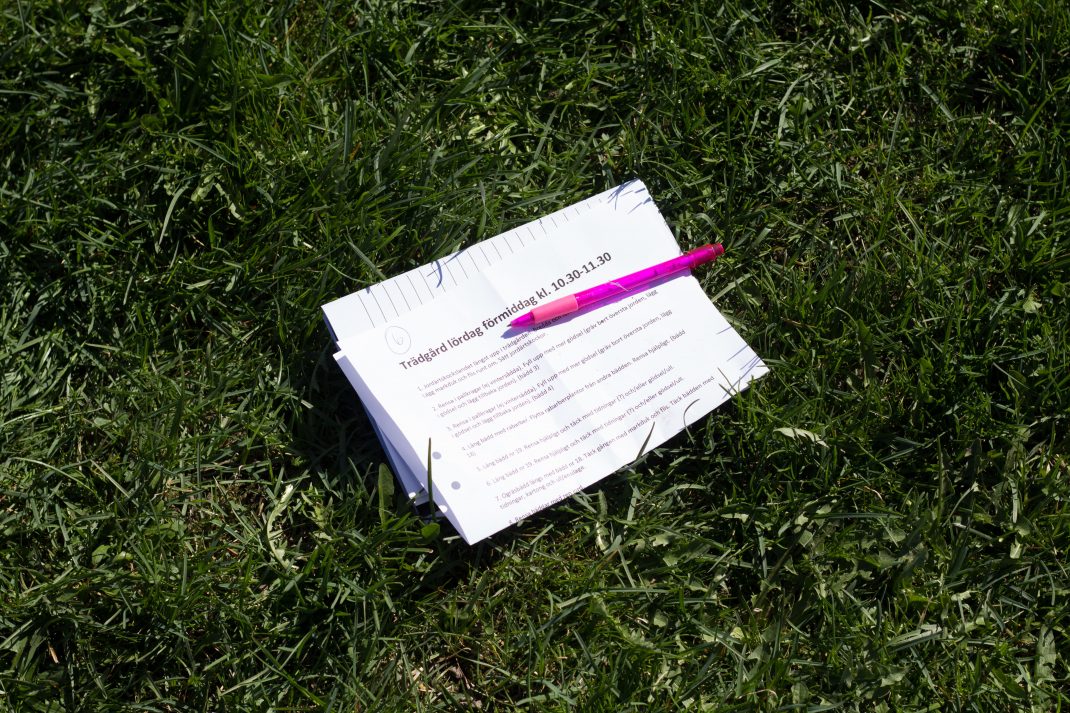 En ihopvikt lista ligger i gräset tillsammans med en rosa penna.