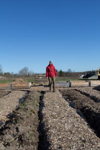 I den stora köksträdgården går Sara i röd jacka och med ett stort leende.