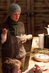 Sara står upp och provsmakar maten vid buffé bordet. I förgrunden av bilden syns ett av barnen ta till sig av maten.