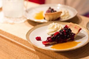 Närbild på en bit kaka med mörkblåa och röda bär, krispig botten, en klick grädde och gyllenbrun kolasås.