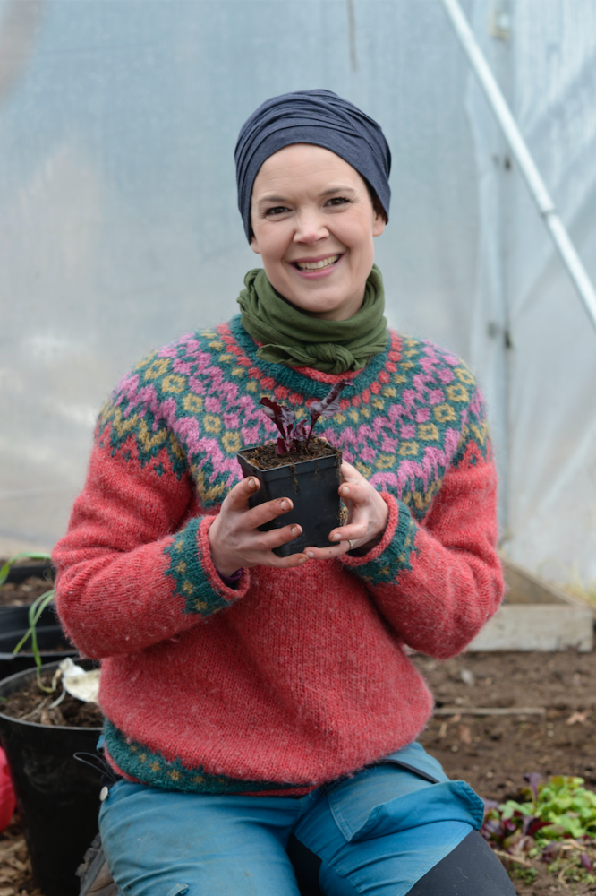 Sara Bäckmo sitter i tunnelväxthuset och håller en liten planta i handen. 