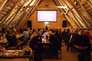 En loge med högt i tak, ljuslytkor och massor av personer som tittar på Sara när hon föresläser.