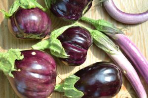 Åtta blanka frukter av aubergine i olika nyanser av lila ligger på ett skärbräde.