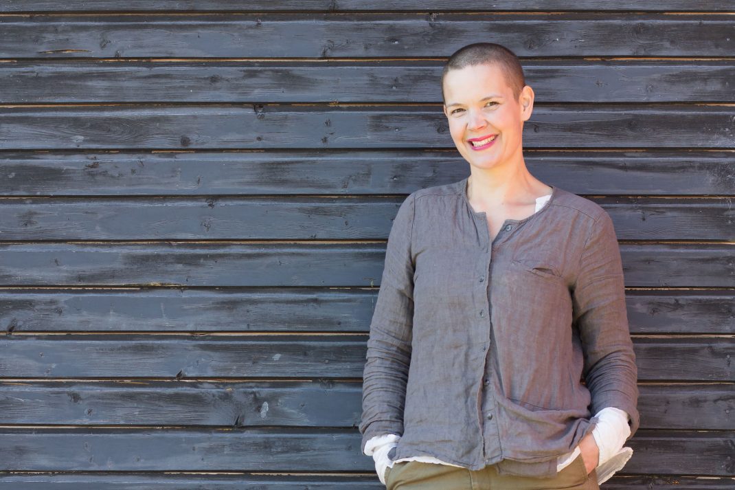 Sara mot en grå ladugårdsvägg med ett stort leende på läpparna. 