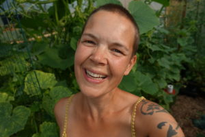 Närbild av Sara, som ser väldigt glad och solbränd ut där hon står inne i växthuset.