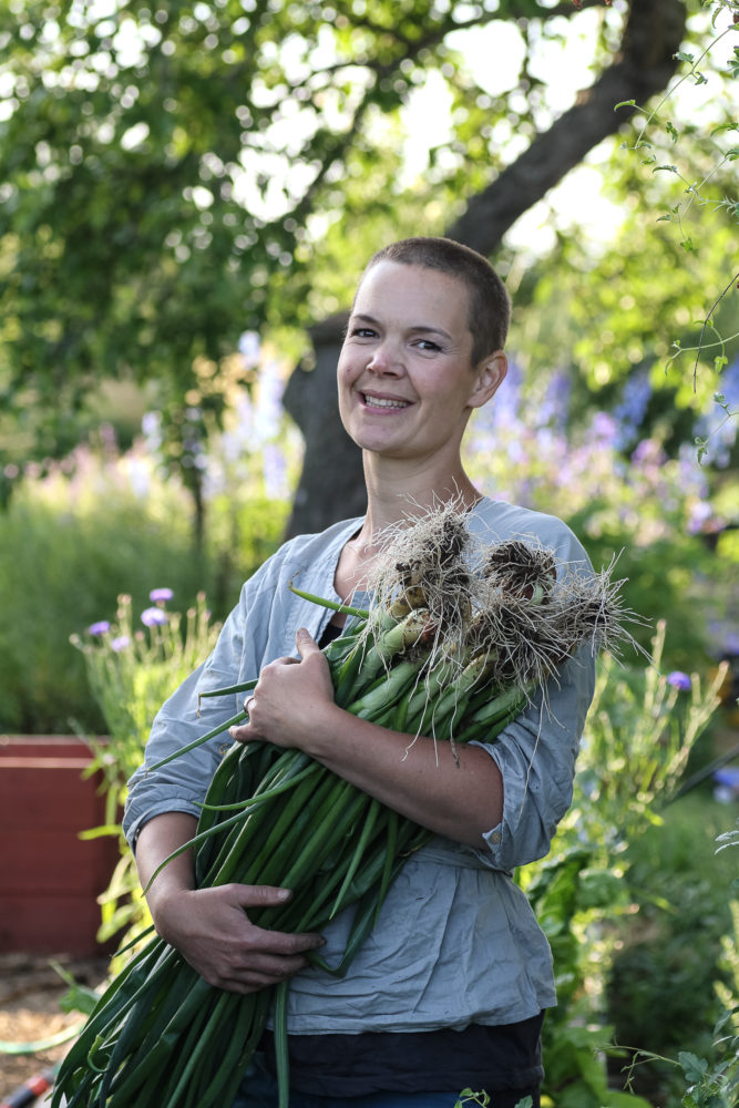 Sara tittar glad in i kameran med ett stort knippe lök i famnen.