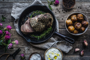 Ett rejält köttsstycke ligger serverad i gjutjärnspanna med örter, potatis och sås som tillbehör.
