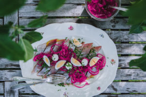 En fin tallrik med grå matjessill. ägghalvor och mörkt rosa lökbitar.