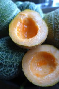 En uppskuren melon ligger med saftigt, oranget fruktkött i en skål.