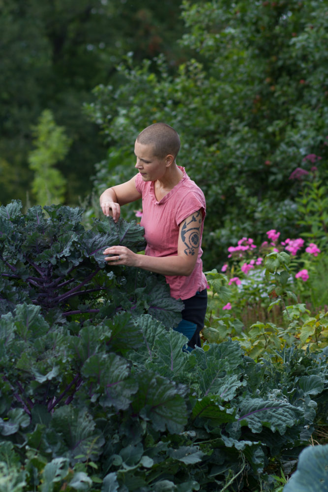Sara i rosa tröja står vid ett maffiga mörkgröna kålplantor som räcker ända upp till bröstet på henne.