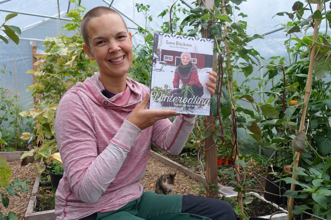 Sara Bäckmo sitter i växthuset och håller den nya boken bredvid sig. 