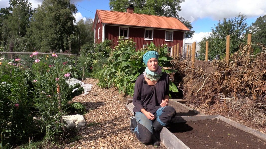 Sara Bäckmo sitter på en kant till en odlingsbädd i en somrig trädgård. 