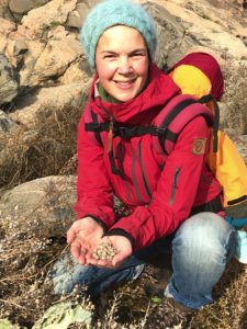 Sara sitter vid en planta och visar frön som ligger i handen.
