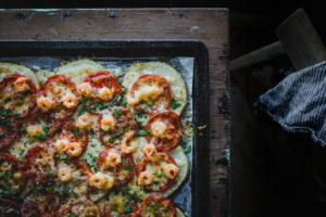 En plåt med gratinerad rotselleri, med skivad tomat och skaldjur.