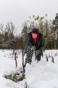 Sara lyfter på ett kompostgaller under snön.