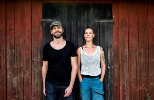 Sara och Johannes står framför en röd ladugård med svart dörr.