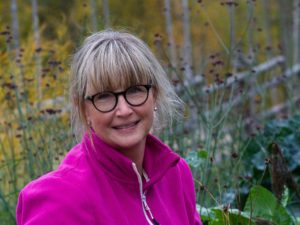 En kvinna i rosa fleecetröja i en färgrik höstträdgård.