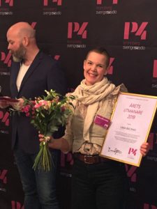 Leende Sara håller diplom och blommor.