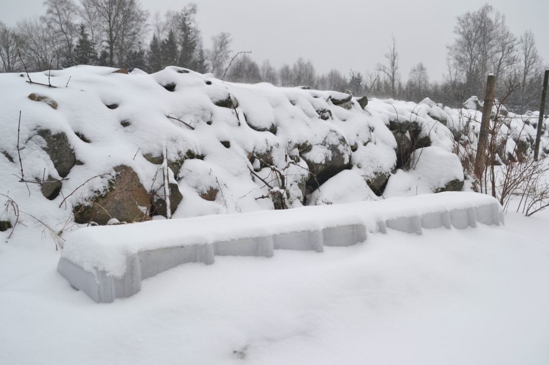 Ett snötäckt landskap med stenmur och ett land som anas under snön. 