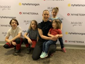 Gruppgild på Sara och barnen framför programloggor på en vägg.