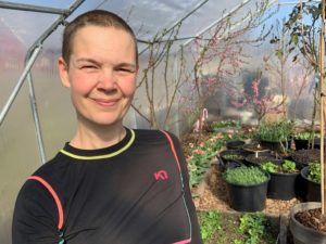 Sara i underställströja står i ett varmt tunnelväxthus.