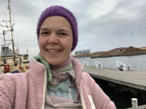 Sara i mössa och rosa jacka vid en kaj vid havet.