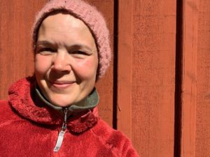 Sara i stickad mössa står mot en röd vägg.