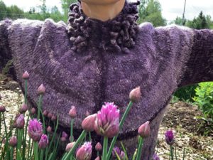 Sara med utfällda armar i lila kofta och gräslöken som blommar i förgrunden.