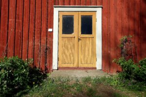 En gul entrédörr mot faluröd trävägg.