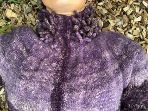 Sara liggandes på flisen och visar koftan framifrån.