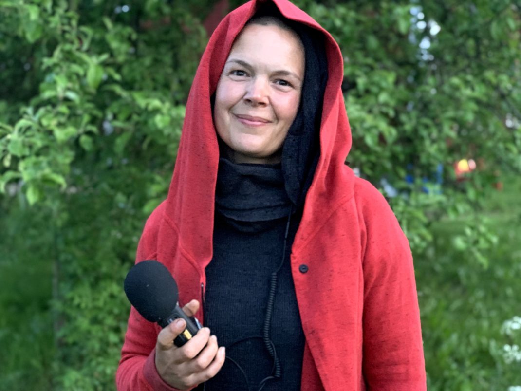 Sara Bäckmo står i trädgården i röd luvtröja och bandare i handen. 