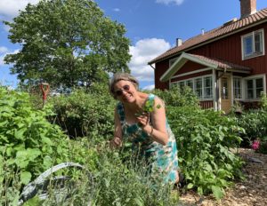 En kvinna i grön mönstrad klänning står bredvid en bädd med kryddor