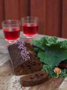 En saftig mörkbrun chokladkaka ligger på ett bord bredvid grönkål och två glas vinbärssaft.
