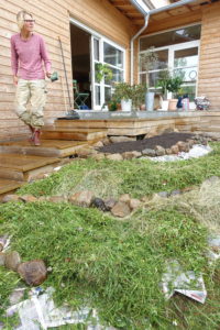 En träfärgad byggnad meden liten kulle nedanför täckt med gräsklipp.