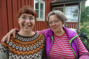 Två kvinnor står bredvid varandra med armarna om varandras axlar.