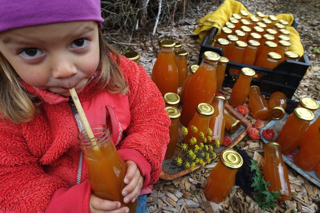 Ett litet barn i färgglada kläder dricker must ur en flaska med sugrör. 